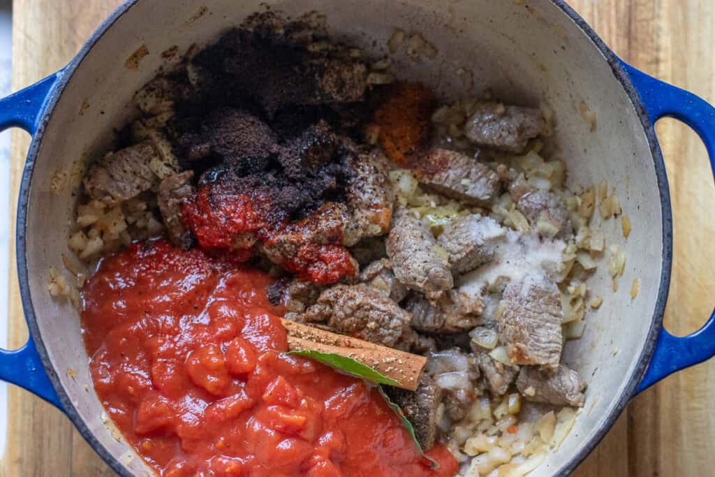 Tomatoes, tomato paste, seasoning, and flavorings are added to the pan.