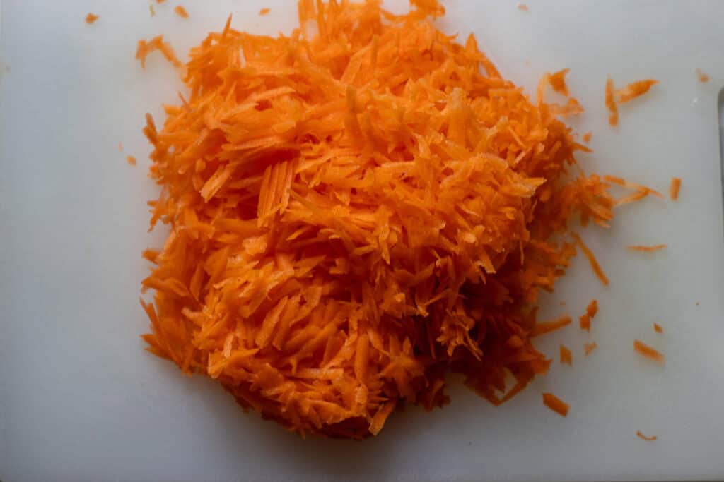Freshly grated carrots on a white cutting board.