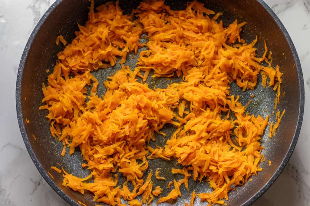 Grated carrots cooking in olive oil in a frying pan.