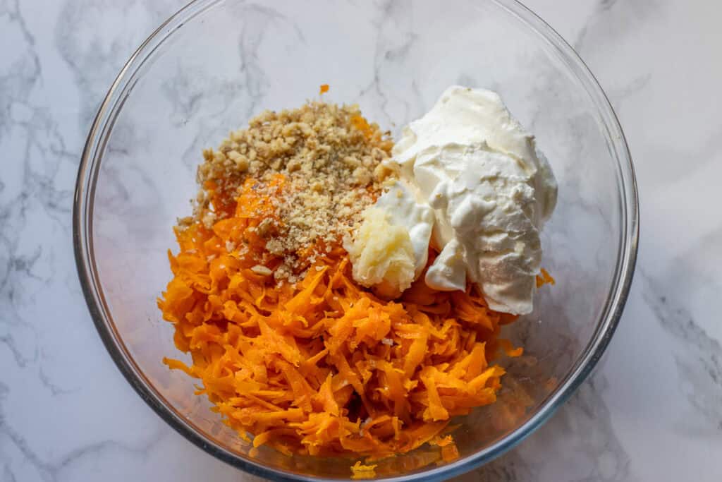 Cooked carrots, crushed walnuts, yogurt and garlic in a glass mixing bowl.