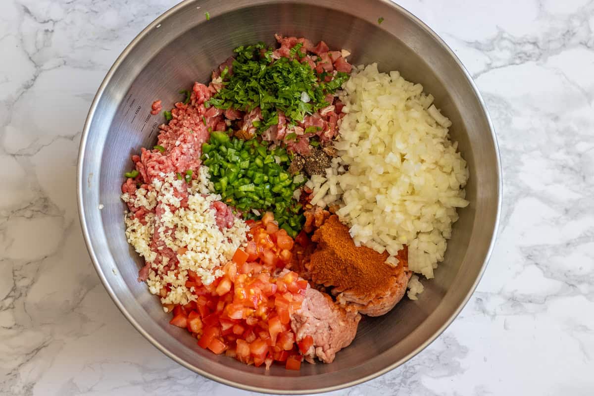 meat, spices, and chopped vegetables are placed in a bowl