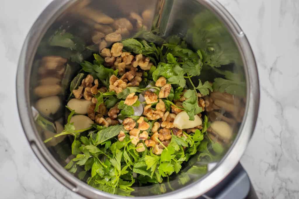 Walnuts, garlic and fresh herbs in a food processor bowl before blending.