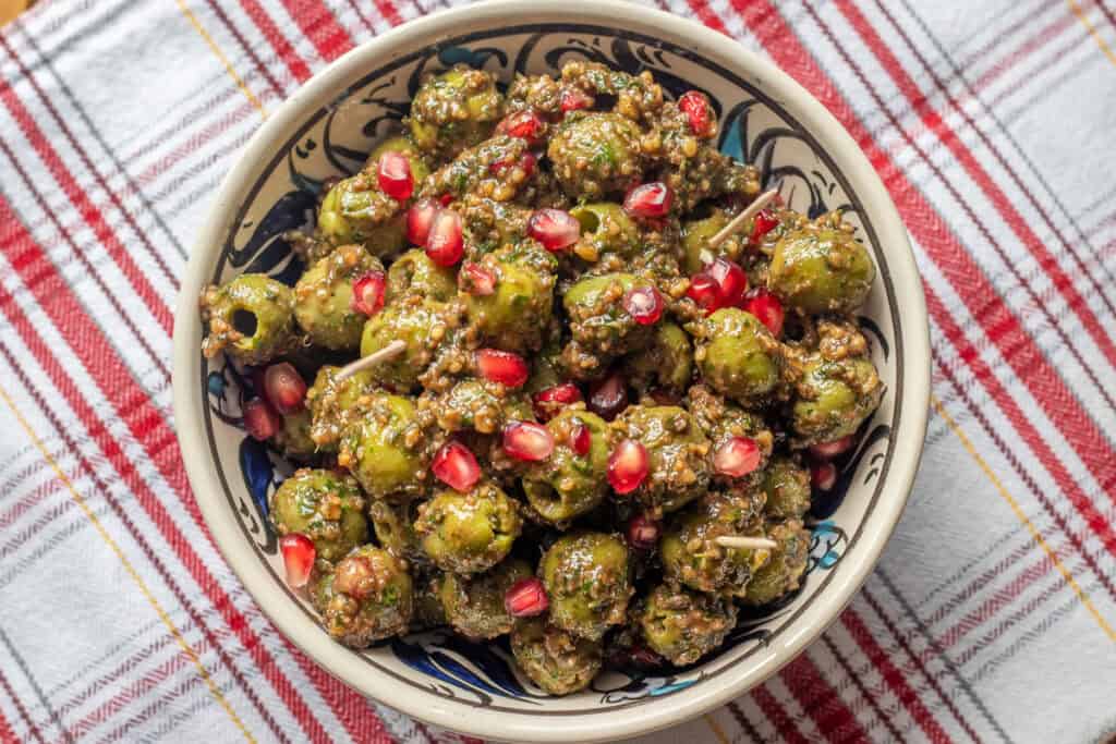 A bowl of finished zeytoon parvardeh on a red striped cloth, topped with pomegranate seeds.