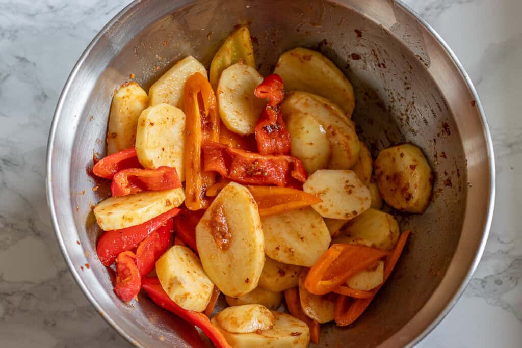 Sliced potatoes and peppers tossed with the marinade in a metal bowl.