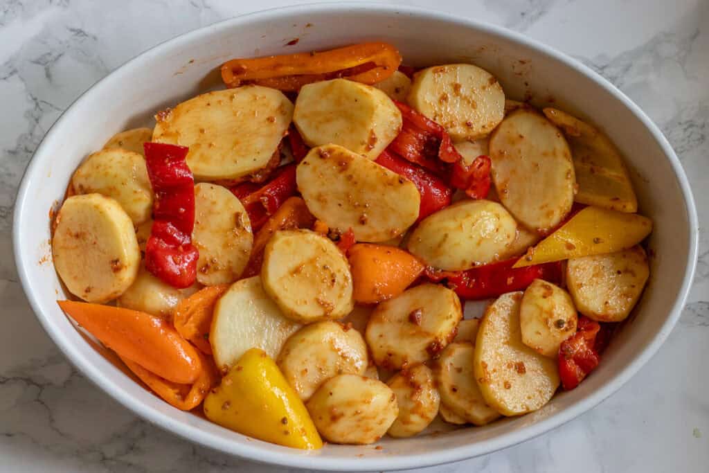 Potatoes and peppers are layered on a baking dish.