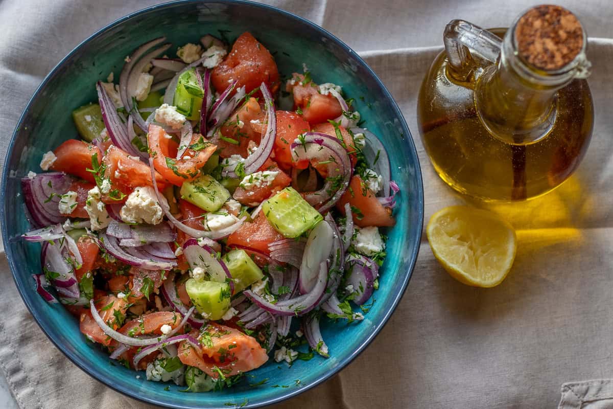 cucumber tomato feta cheese salad served in a bowl with olive oil and lemon wedges