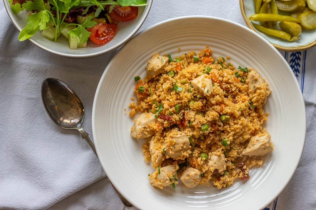 Chicken couscous served in a bowl with salad and pickles on the side.