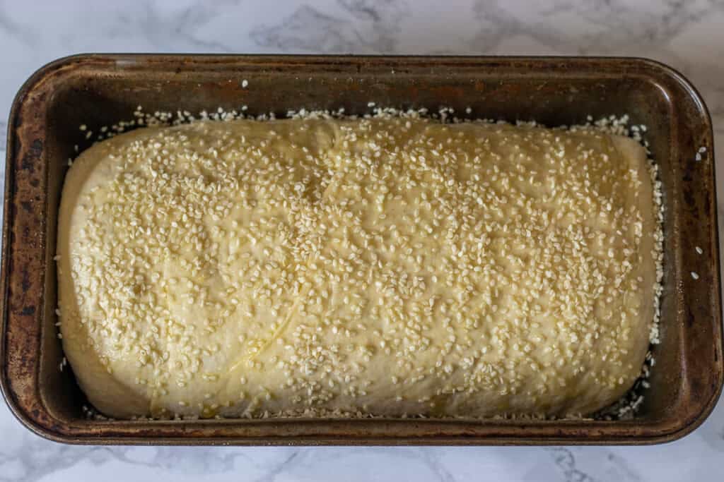 The bread loaf is sprinkled with sesame seeds after the second rise.