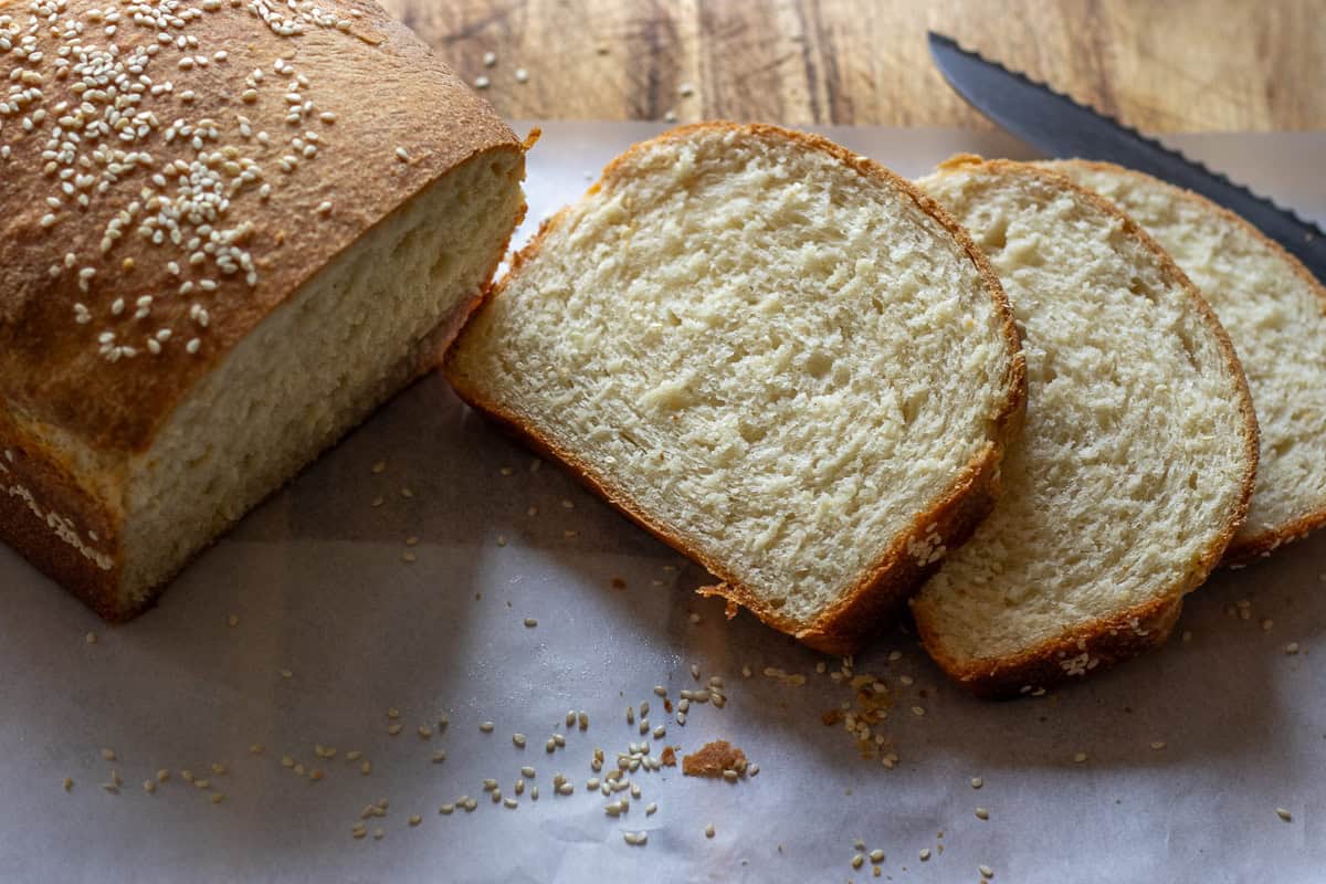 3 Greek bread slices and a knife on a brown cutting board.