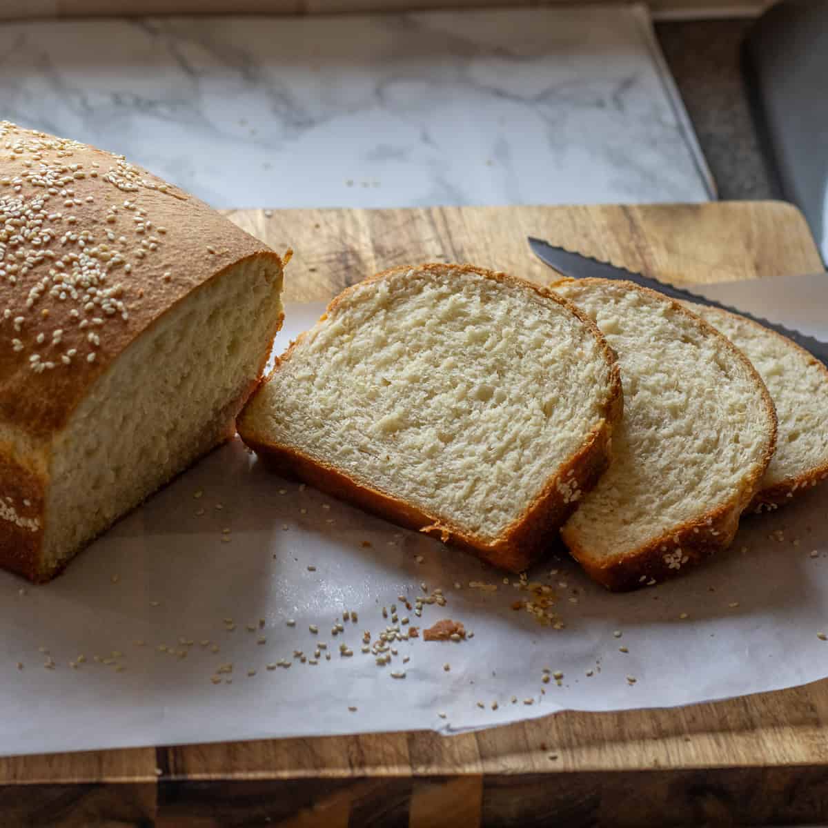 Greek bread with sesame seeds, sliced on a wooden board.