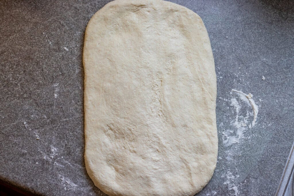 The dough ball is gently pressed into a rectangular shape.