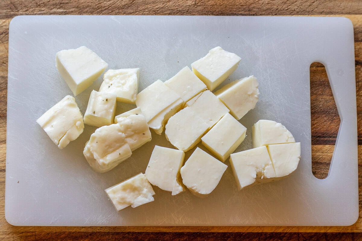 Block of halloumi cheese cut into cubes on a white cutting board.