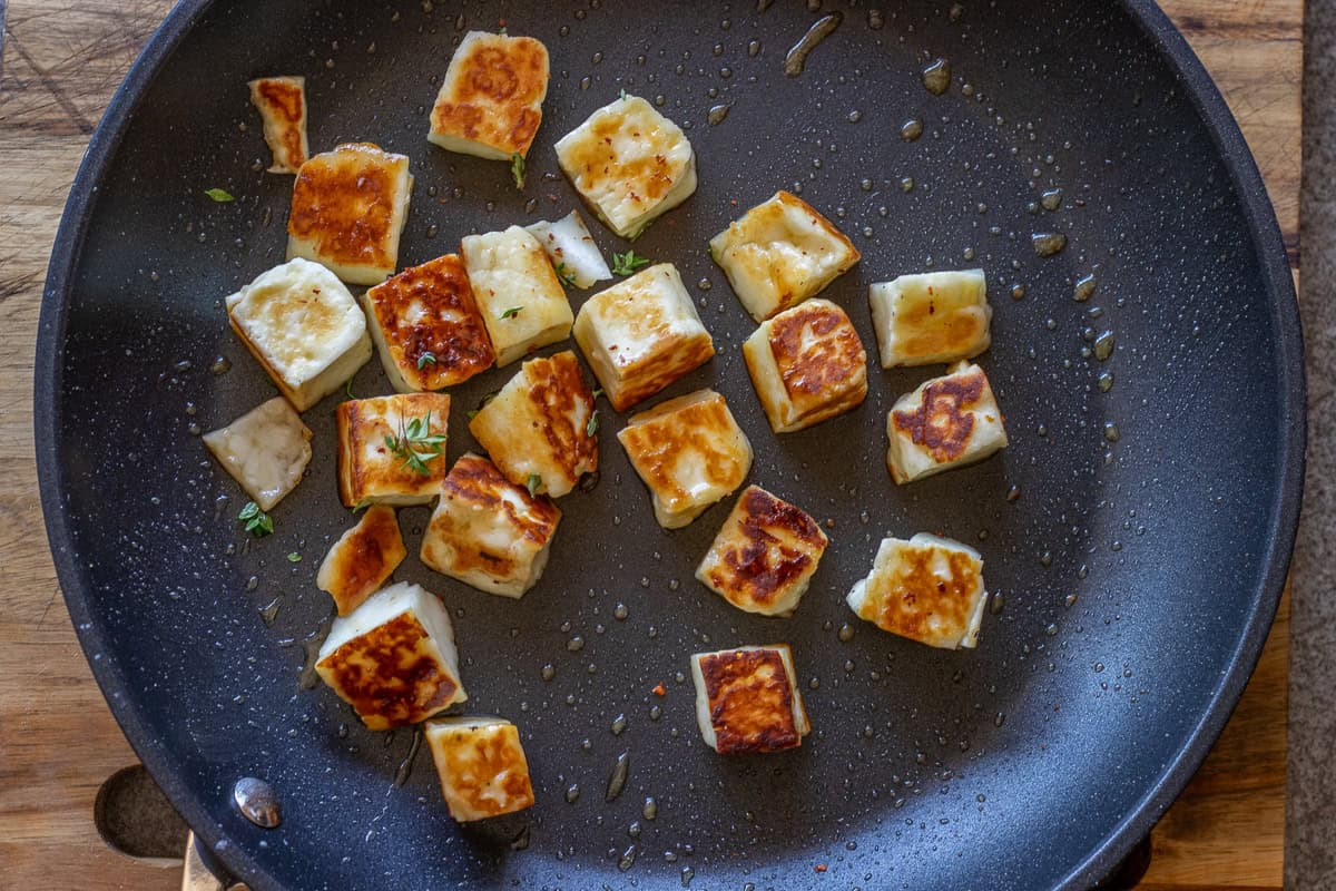 A drizzle of honey, fresh thyme leaves, and a few chili flakes are added to fried halloumi pieces.