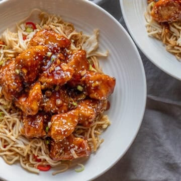 Crispy chicken pieces coated with honey and sesame, served on noodles.