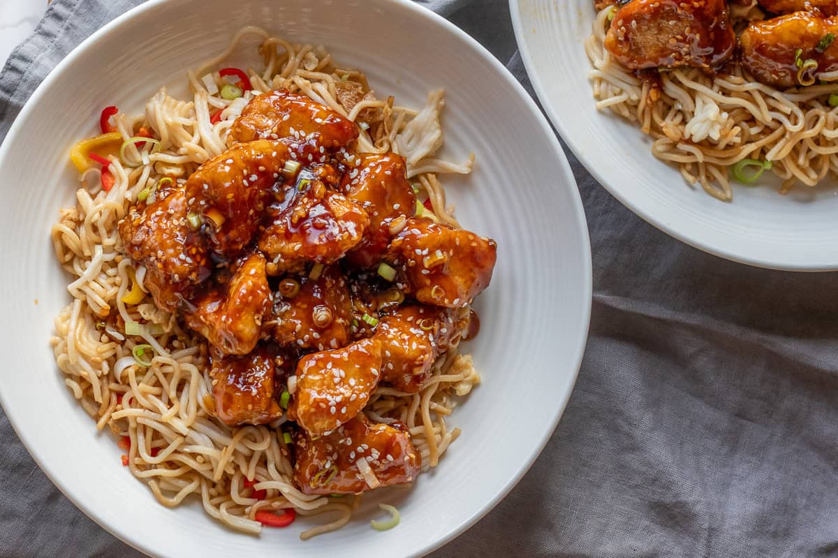 Crispy chicken pieces coated with honey and sesame, served on noodles.