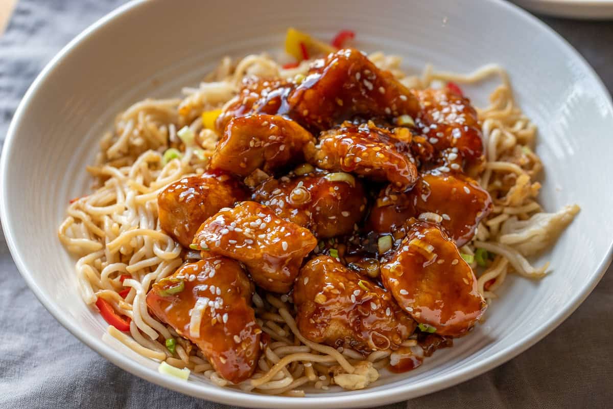 Crispy honey sesame chicken pieces served over noodles.