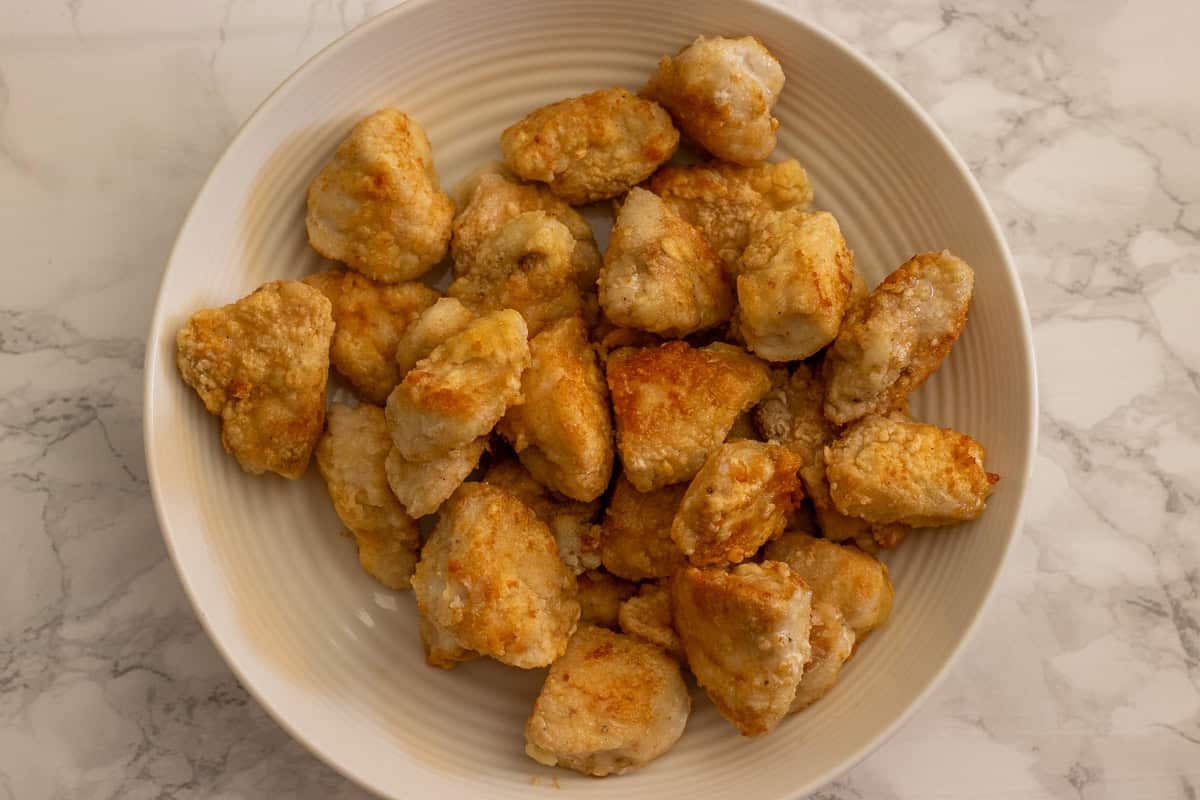 Coated chicken cubes are fried until golden and crispy.