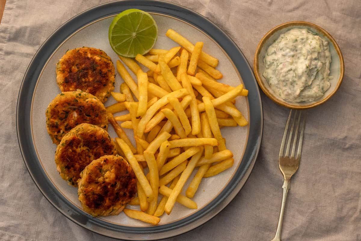 Salmon patties served with french fries, half a lime, and a bowl of tartar sauce.