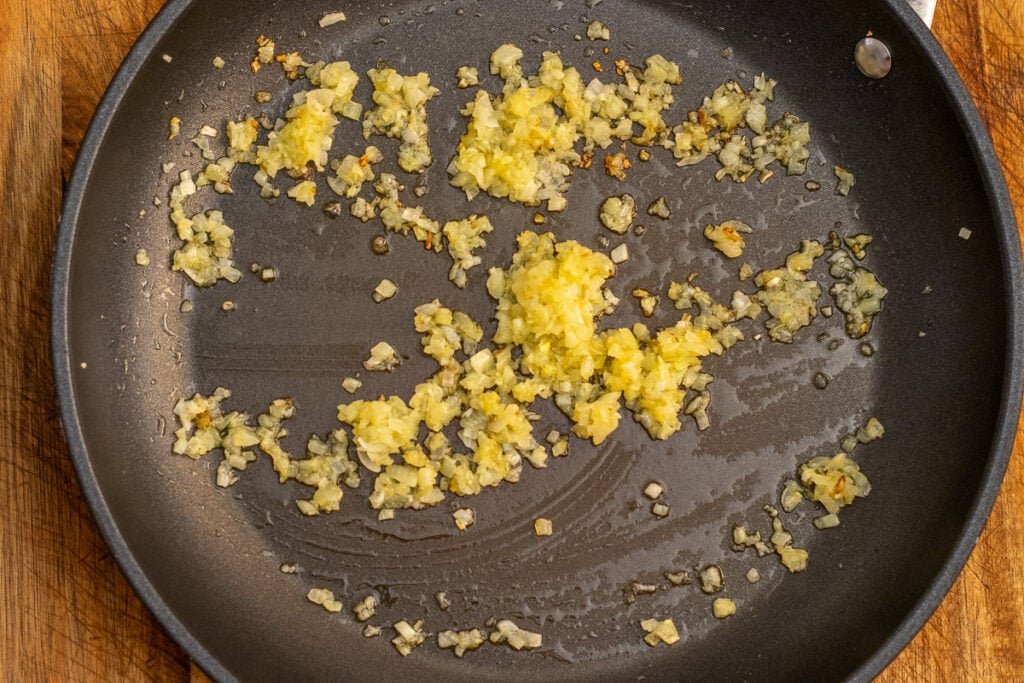 Finely chopped onion and garlic cooking in olive oil in a frying pan.