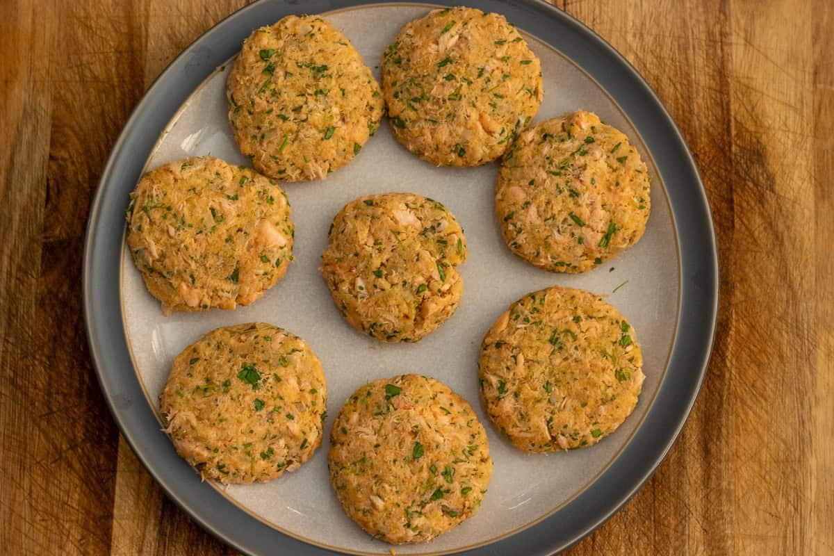 Eight shaped raw salmon patties on a gray plate.