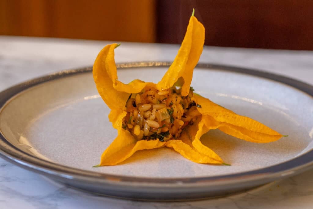 A single zucchini flower stuffed with rice filling on a plate.