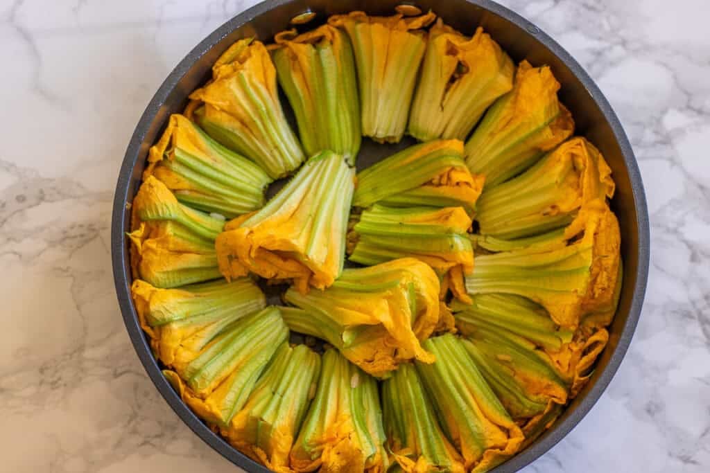 Stuffed zucchini flowers arranged closely in a pot before cooking.