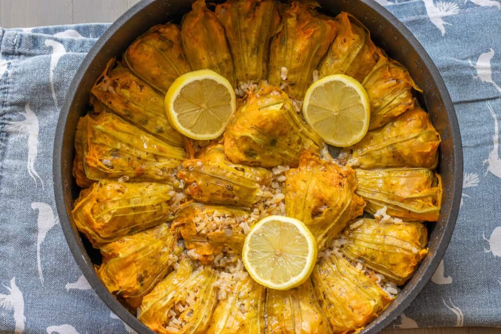 Cooked stuffed zucchini flowers in a pot, garnished with lemon slices.