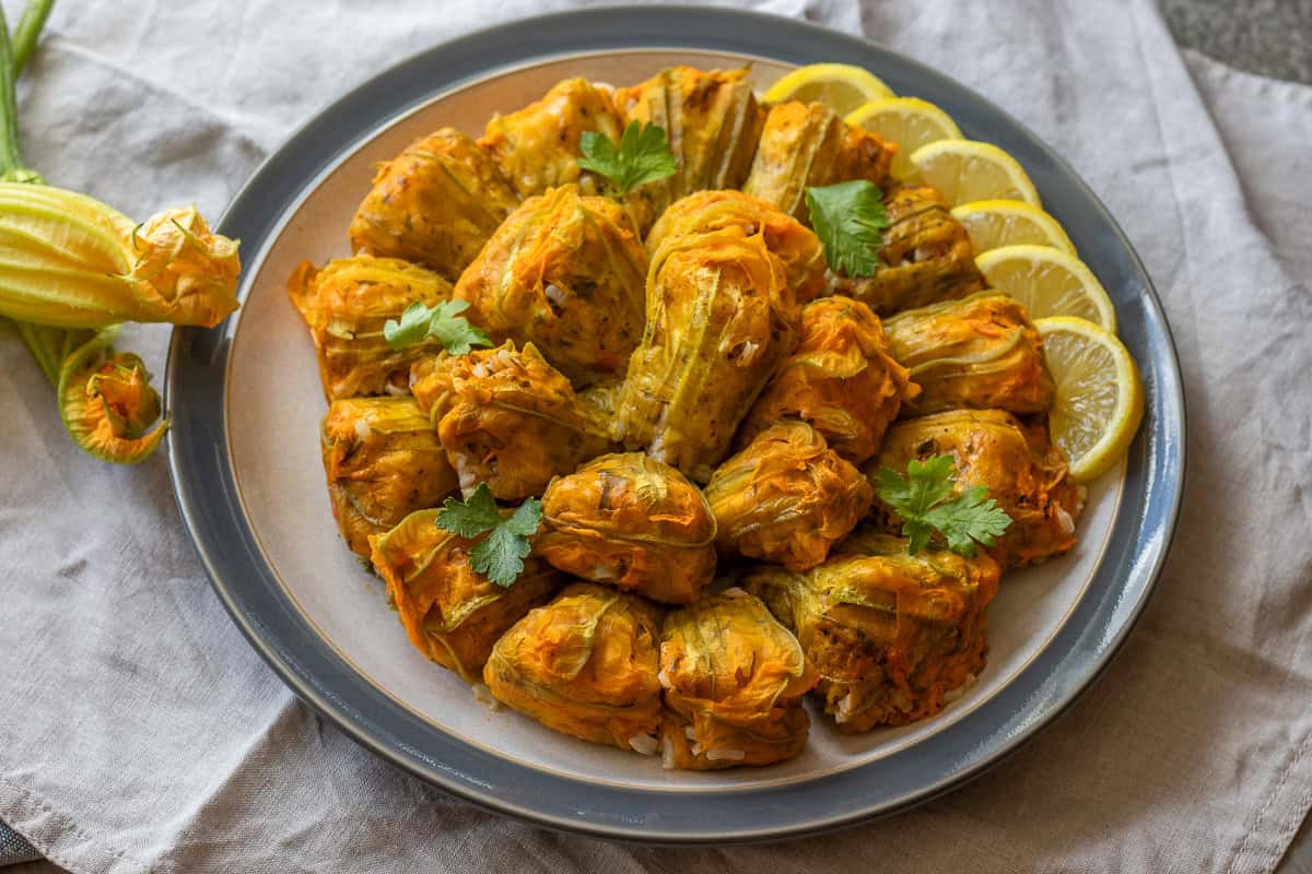 Stuffed zucchini flowers arranged on a plate with lemon wedges and fresh herbs.
