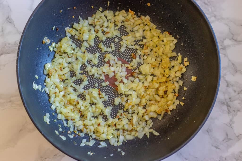 Diced onion and rice cooking together in a pan.