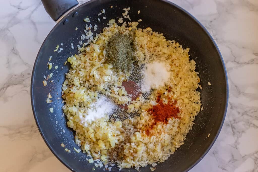 Rice topped with salt, pepper, and paprika in a pan before stirring.