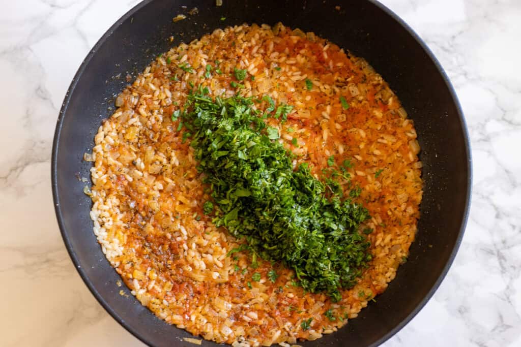 Tomato rice filling topped with chopped fresh herbs in a pan.