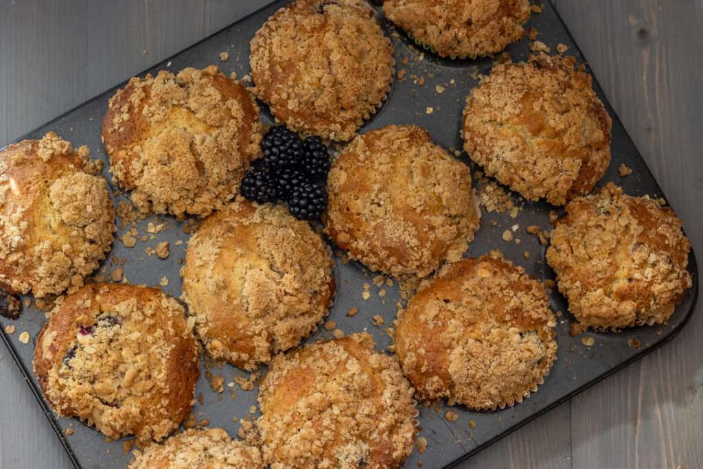 Baked muffins on a baking tray with a pile of fresh blackberries.
