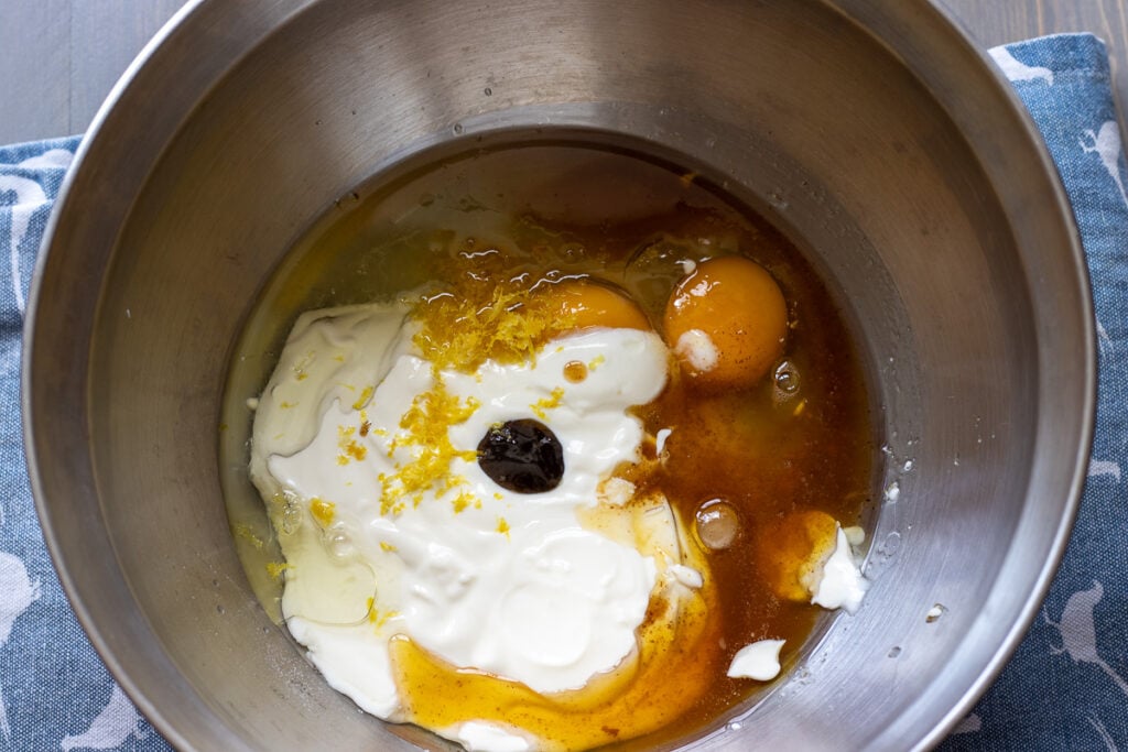 Eggs, yogurt, oil, and lemon zest in a mixing bowl.