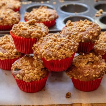 Freshly baked muffins with a crunchy oat topping stacked in red liners.