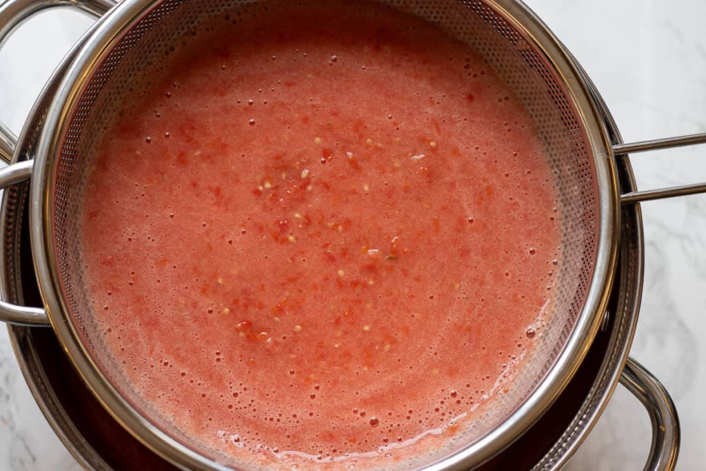 Blended tomatoes in a fine sieve over a pot.