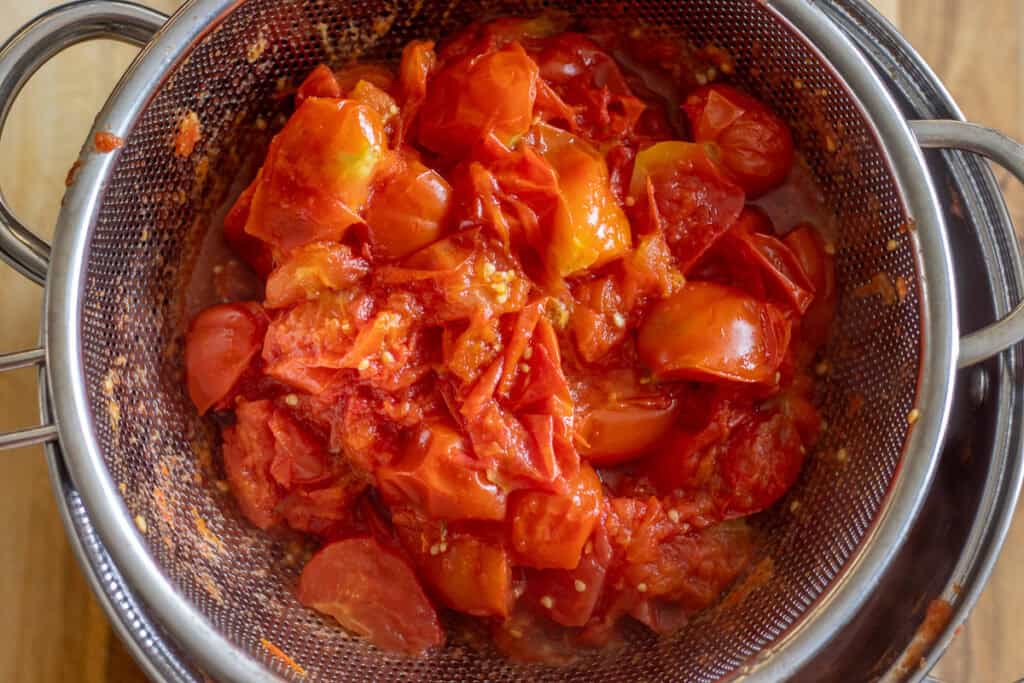 Soft boiled tomatoes draining in a sieve.