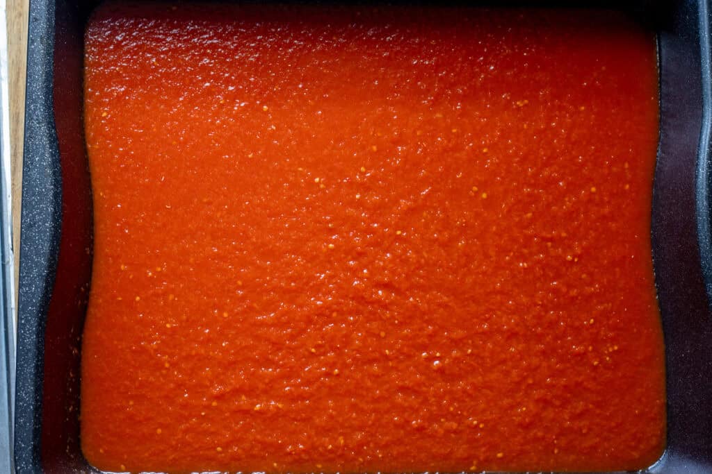 Partly reduced tomato sauce spread on a large tray.