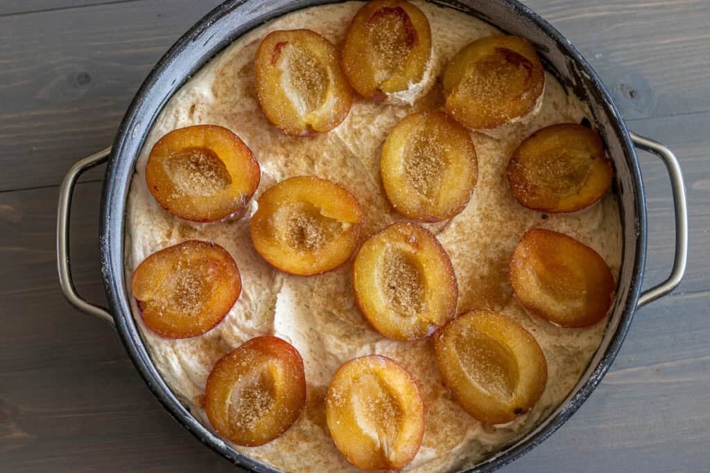 Halved plums arranged cut-side up on the batter with sugar on top.